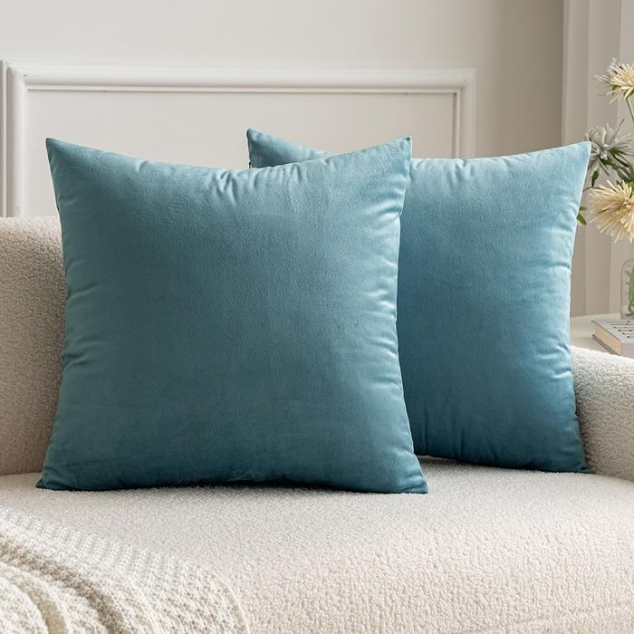 Two light green velvet square throw pillows arranged on a couch