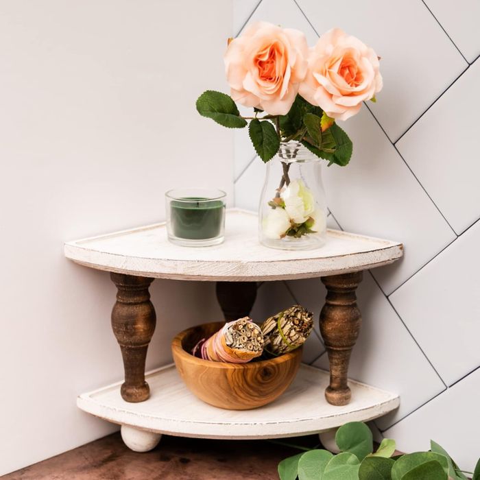 A corner shelf showcasing decorative items such as a vase with roses, a candle, and a bowl filled with ornaments