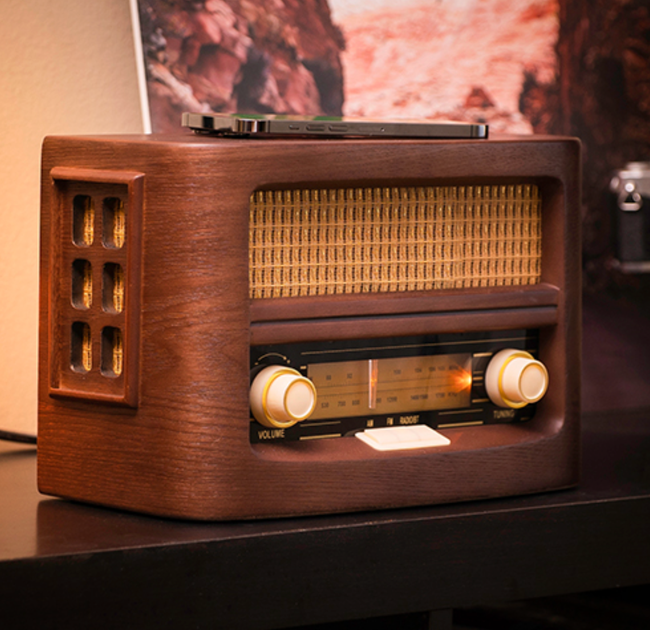 Vintage-inspired wooden radio with classic dials and manual tuning, with a phone charging on top