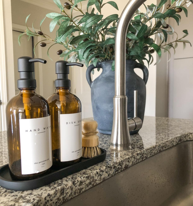 A reviewer’s neatly arranged bottles for hand soap and dish soap placed on a matte black oval tray