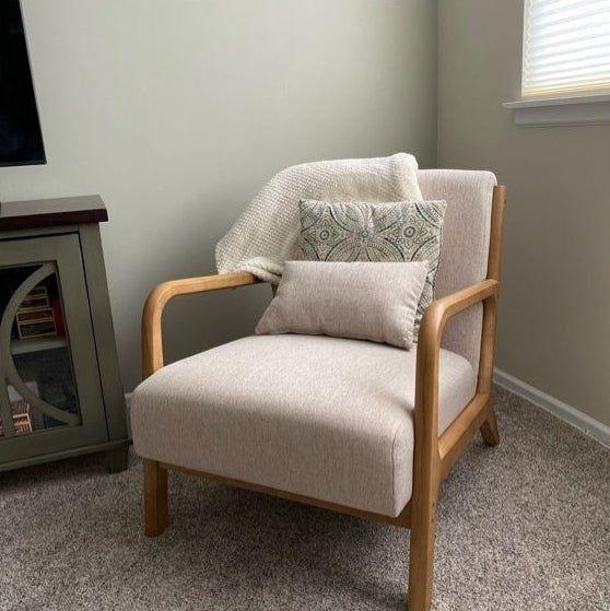 A modern armchair with a beige cushion and throw pillow, positioned by the fireplace and beneath a window.