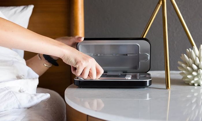 A hand reaching into the PhoneSoap box (a UV sanitizing station for phones) to pick up the phone.