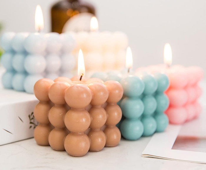 The beige, blue, and pink candles neatly arranged together with their wicks flickering