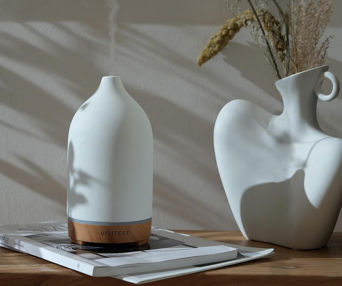 A diffuser placed next to a white vase filled with faux flowers