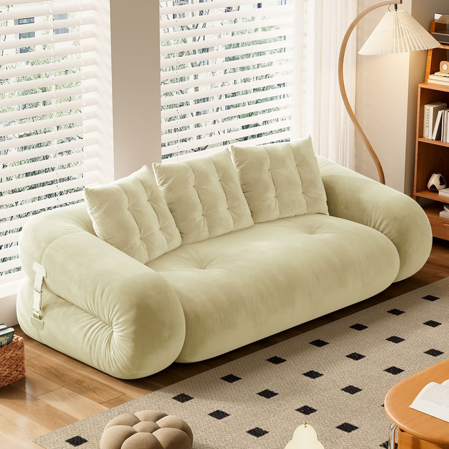Modern plush sofa with rounded arms and multiple cushions in a bright living room, featuring a patterned rug and bookshelf