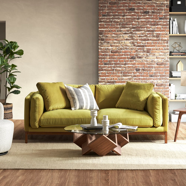 A stylish, contemporary living room featuring a green sofa, a geometric wooden coffee table, and a brick accent wall. It's the perfect inspiration for home decor shopping.