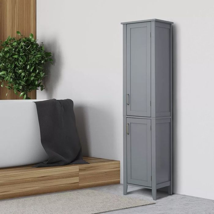 A tall grey storage cabinet with double doors, positioned beside a bathtub on a wooden platform, accompanied by a green potted plant nearby.