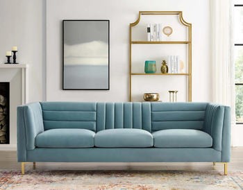 soft gray-blue sofa with gold legs and plush cushions. The upright back features both horizontal and vertical tufting.