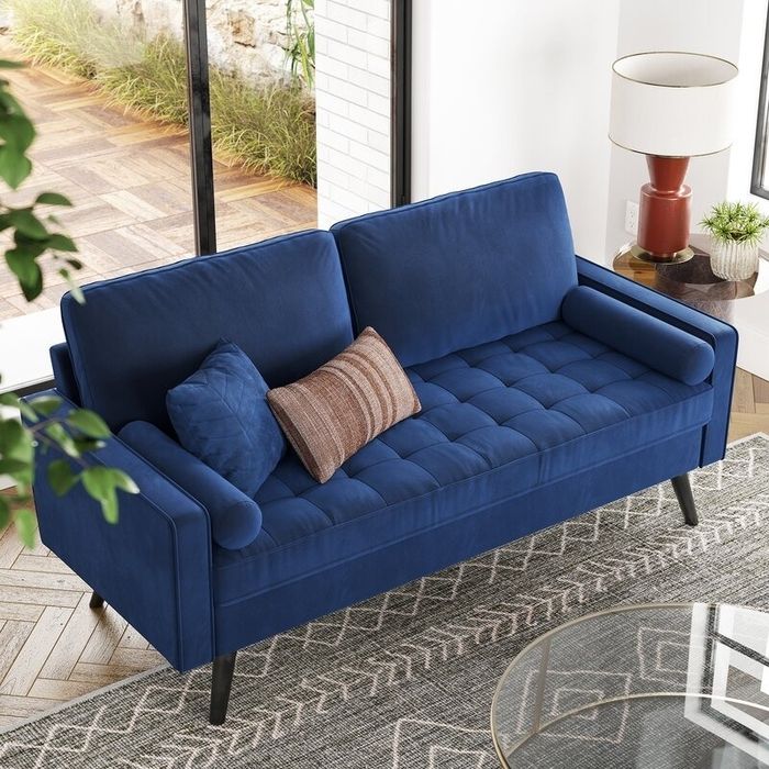 A contemporary blue sofa with tufted cushions and two decorative pillows, positioned in a bright, sunlit room next to a large window