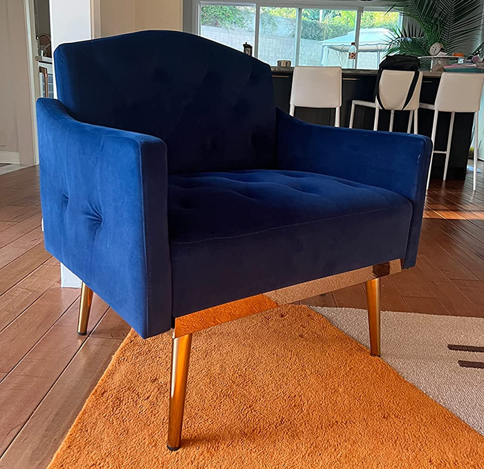 A reviewer’s image showing the side view of a product in cobalt blue with gold metal legs, resting on top of an orange and white carpet.