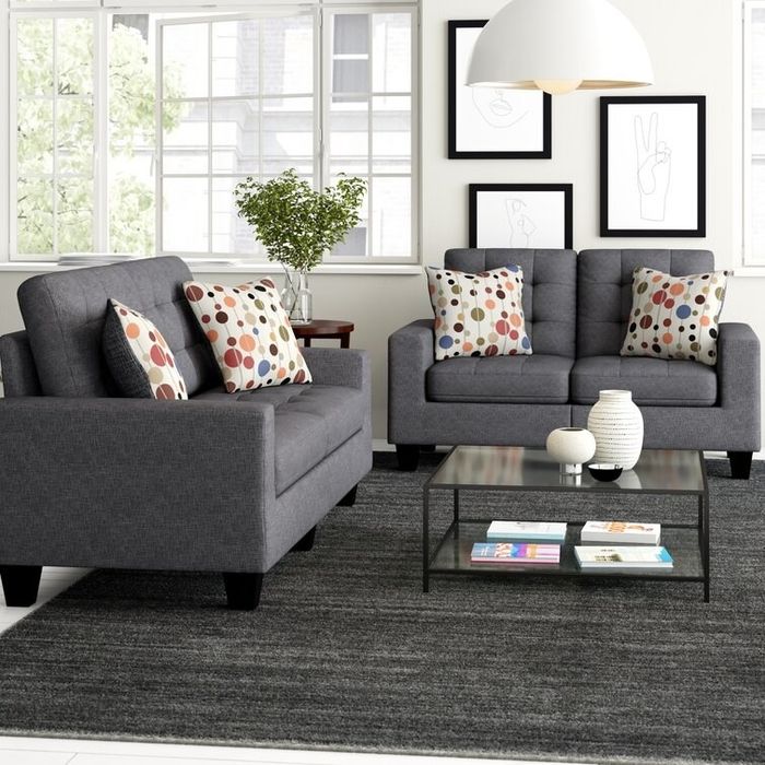 Two sleek gray couches placed on a dark gray rug with a glass coffee table at the center