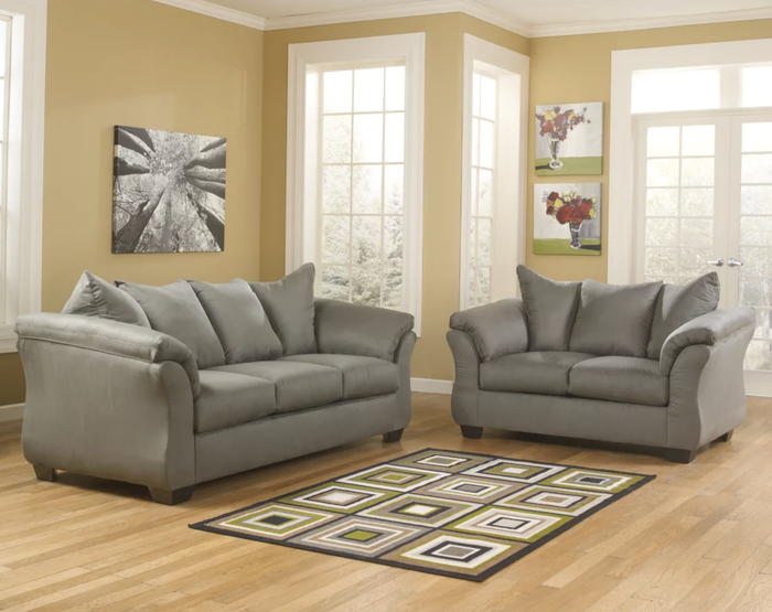 Two gray polyester sofas surrounded by a rug with green, white, and brown geometric patterns