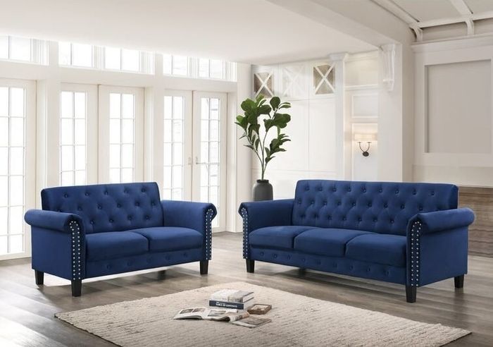 Two blue velvet sofas surrounding a cream rug with a stack of books in the middle