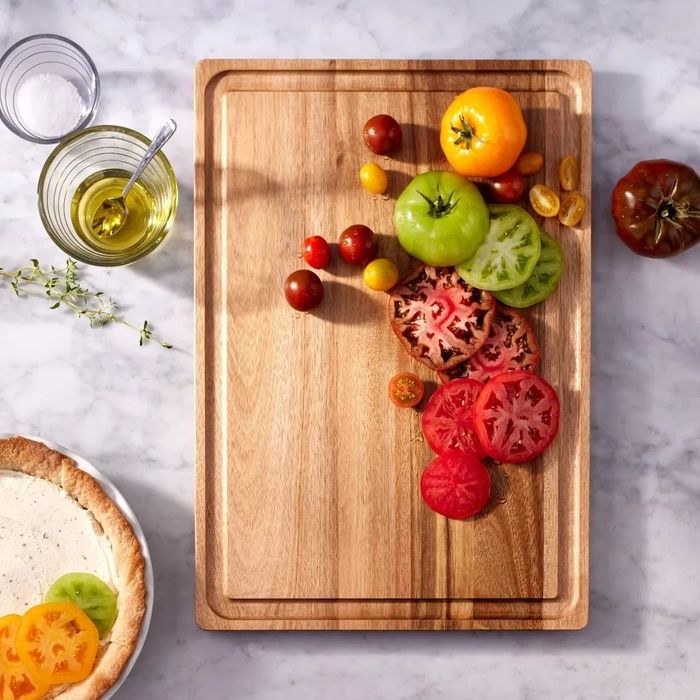 A wooden cutting board with sliced heirloom tomatoes. Nearby are olive oil, salt, and a pizza crust, hinting at a fresh, homemade recipe in the making