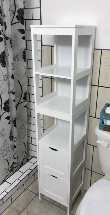 A white linen tower featuring three shelves and two drawers, placed neatly in a bathroom for added storage.