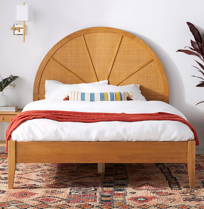 A wooden bed frame featuring a gently rounded cane headboard, offering a warm and natural aesthetic.