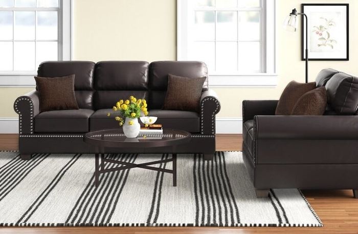 Two brown faux leather couches surrounding a white and brown striped rug and a coffee table