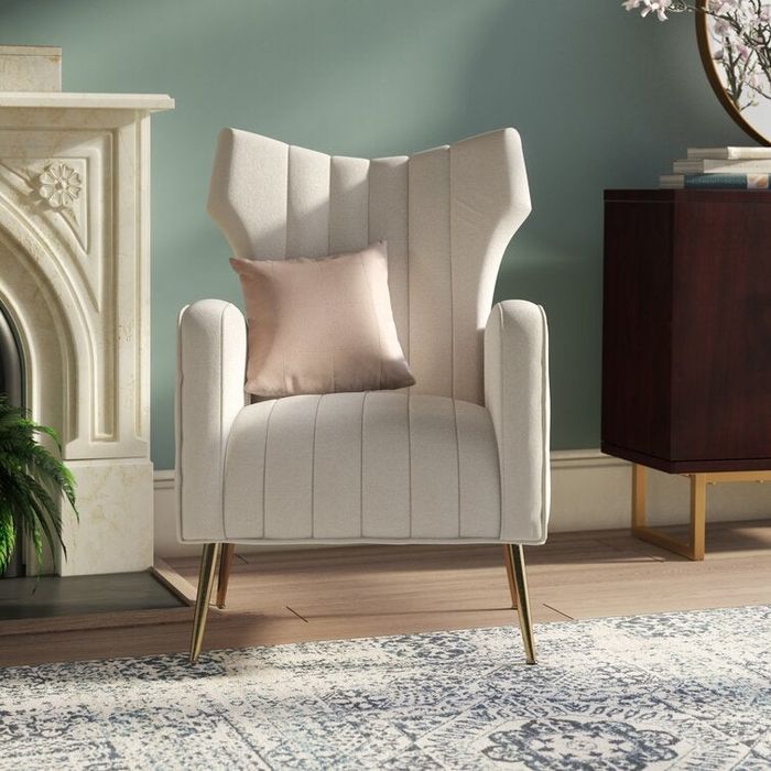 A white velvet wingback chair adorned with a cream-colored throw pillow.