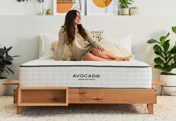 A woman lounging on an Avocado Green Mattress, resting peacefully on a bed frame with an attached bookshelf, offering both comfort and convenience.