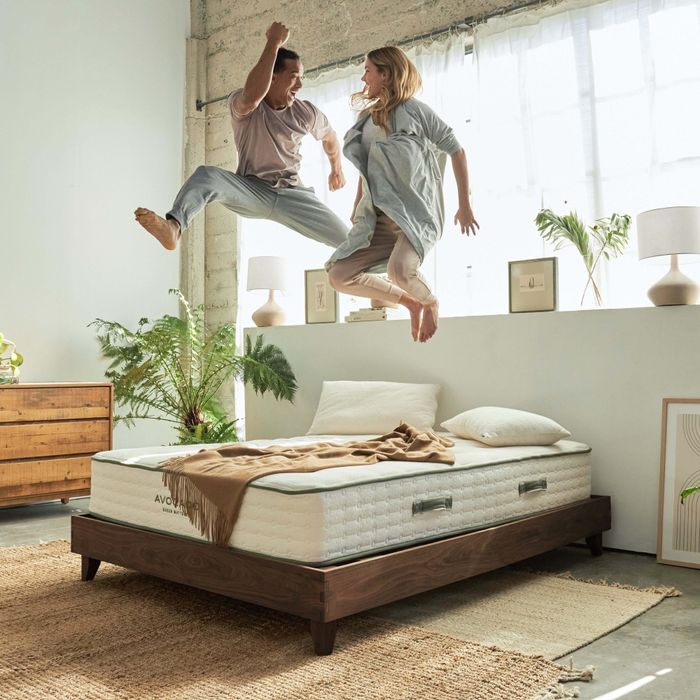 A couple joyfully jumping on an Avocado Green Mattress resting on the sturdy City Bed Frame, embracing comfort and sustainability.