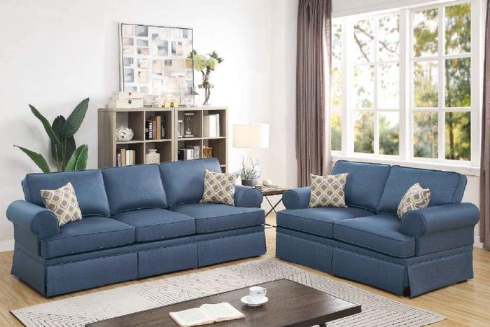 Blue sofa and loveseat with yellow and gray accent pillows, set on a cream-colored rug with a brown coffee table in the center