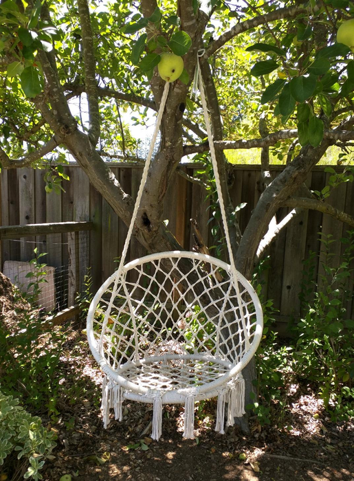 A reviewer’s image showing a white macrame saucer chair hanging from an apple tree.