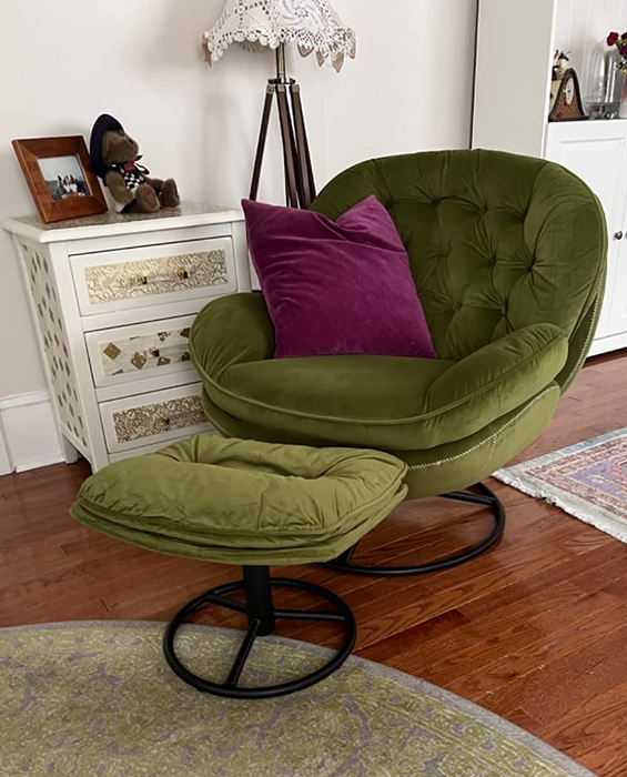 A green, wide, rounded armchair paired with a small ottoman, featuring a sleek black metal circular stand and accented with a vibrant purple throw pillow.