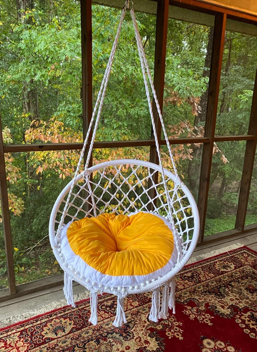 A reviewer’s image of a white macrame chair with an orange and white cushion hanging.