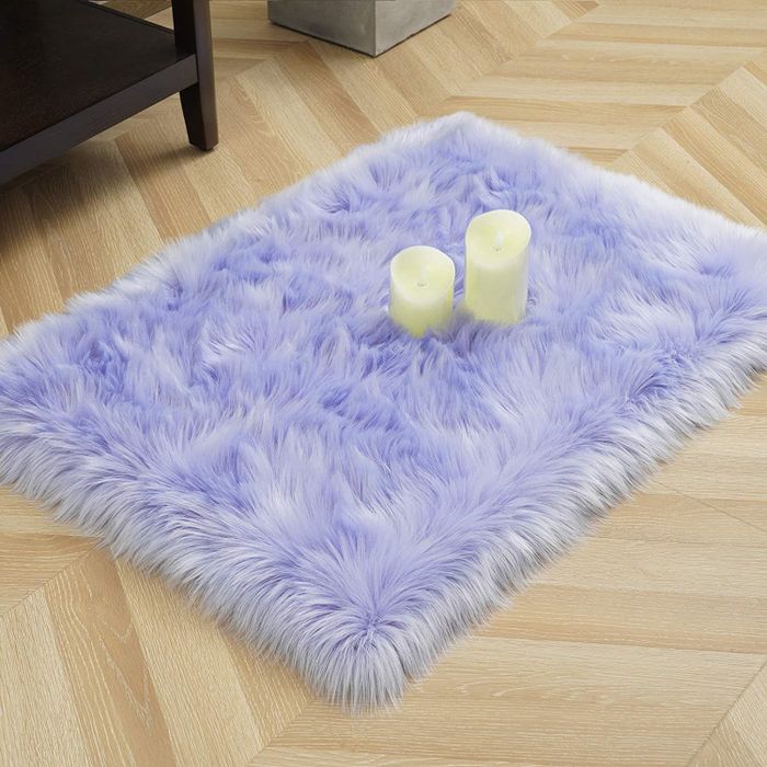 A soft lavender fuzzy rug with two candles resting atop it.