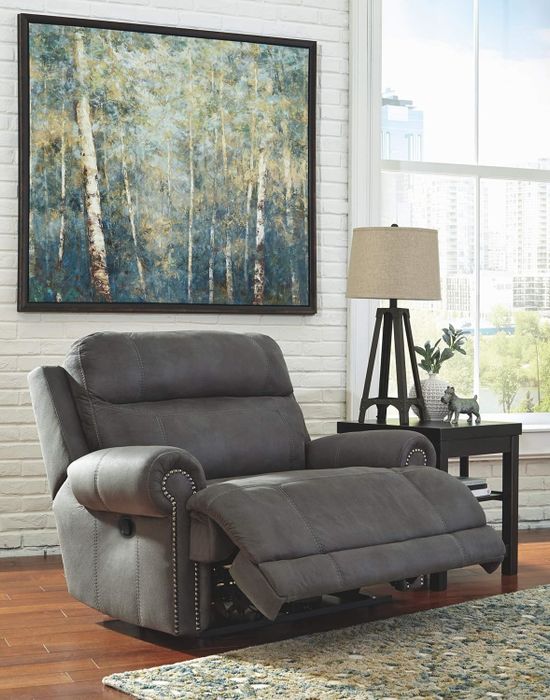A modern living room featuring a leather reclining armchair, a side table with a lamp and decorative items, and a nature-themed painting on the wall.