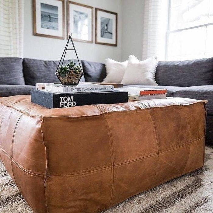 A large brown leather ottoman with books and a plant stacked on top of it.