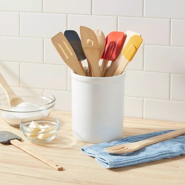 Wooden kitchen utensils with vibrant silicone tips arranged in a white container on a countertop, next to a cloth and small baking bowls