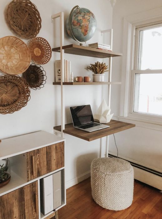 A white and wood wall-mounted desk with two shelves, a computer, lamp, books, and decorative items arranged on it.