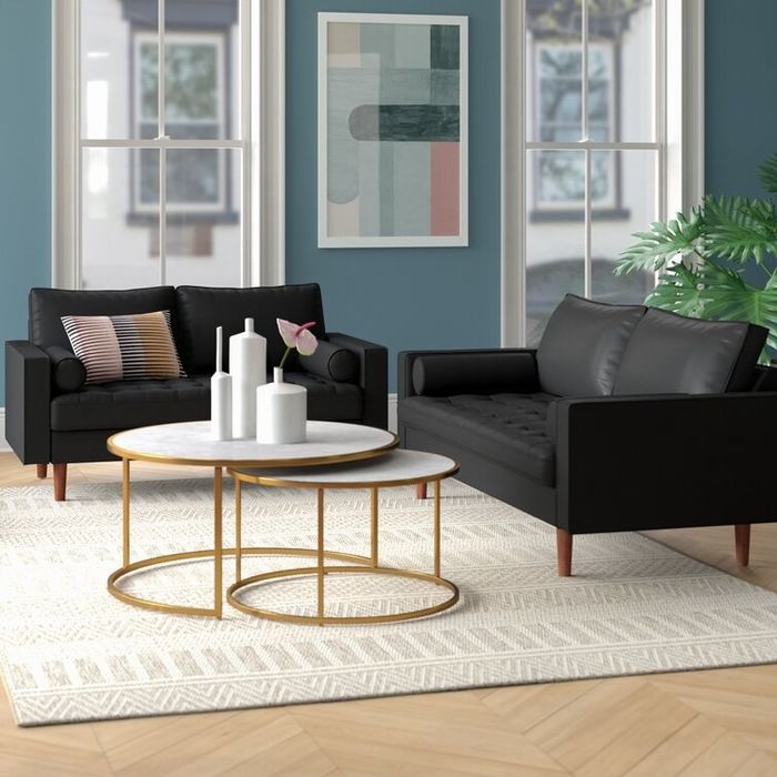 Two sleek black sofas surrounded by two white and gold circular coffee tables