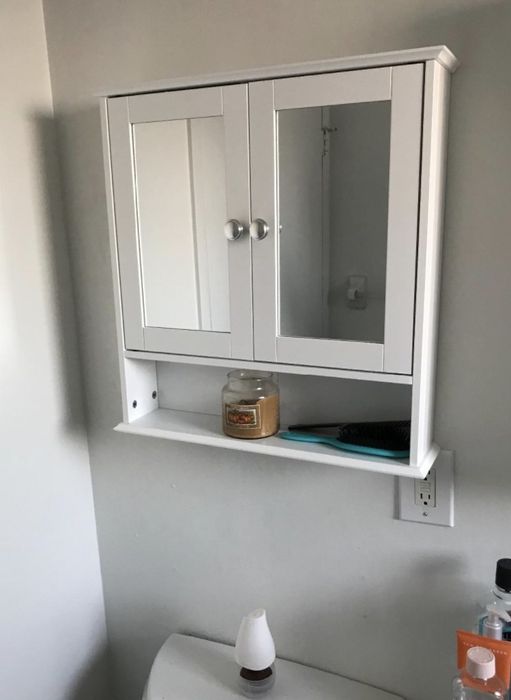 A white medicine cabinet featuring doors and an open shelf for added storage.