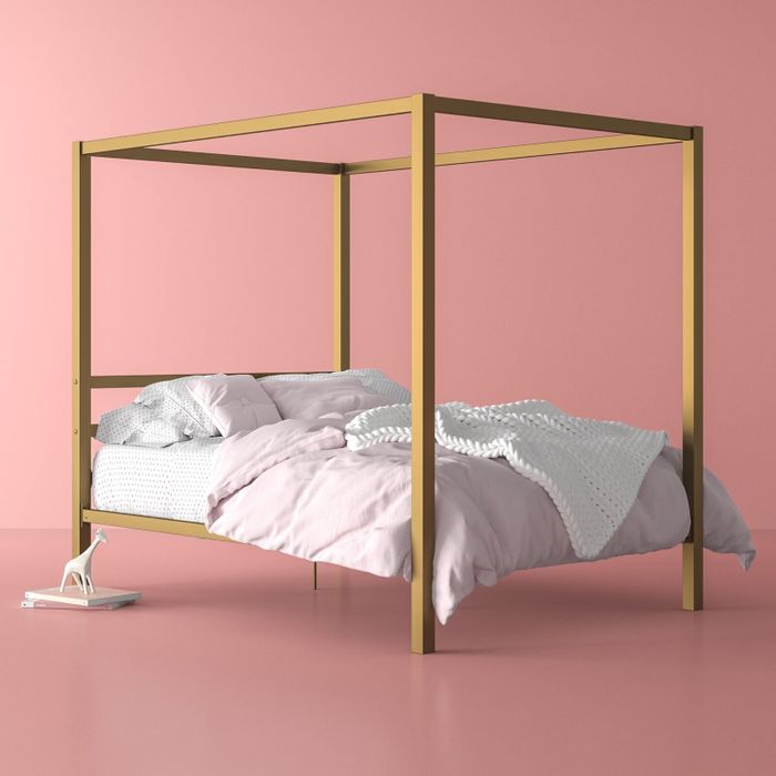 A gold bed frame with the corners of the frame connecting above the bed.
