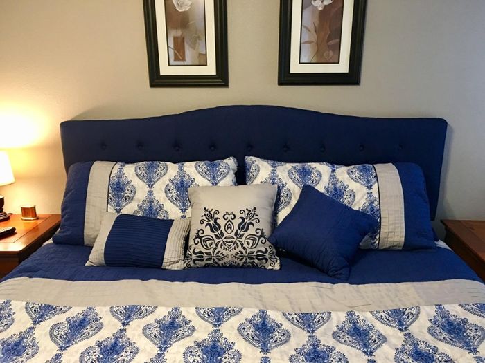 A blue tufted headboard with a gentle curve, placed on a queen-sized bed, offering a stylish touch to the room.