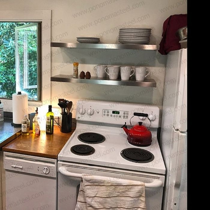 A kitchen featuring stainless steel shelves mounted above the oven.