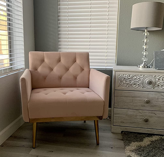 A reviewer’s image showcasing a pink tufted velvet chair with gold metal legs beside a white and gray side table.