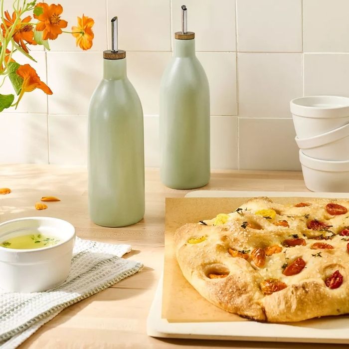 A freshly baked focaccia topped with tomatoes sitting on a wooden board, accompanied by olive oil bottles and a dish of dipping oil on the kitchen counter