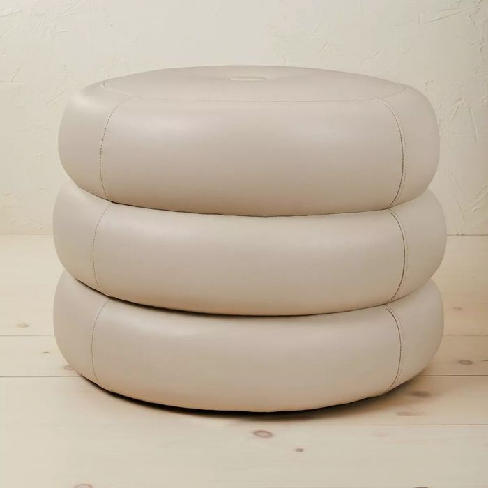 A beige, stackable ottoman with a soft, rounded shape, ideal for both enhancing your home decor and providing extra seating.