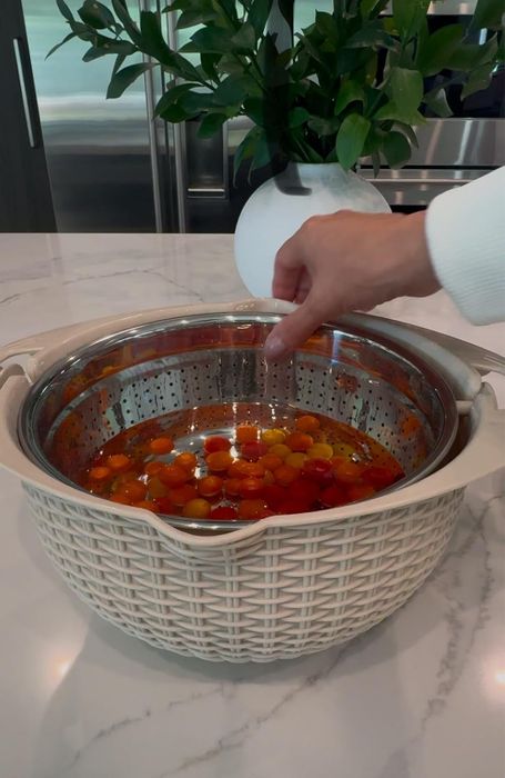 Rinsing tomatoes in a white, woven-patterned colander on a marble countertop, with a plant in the background adding a fresh touch.