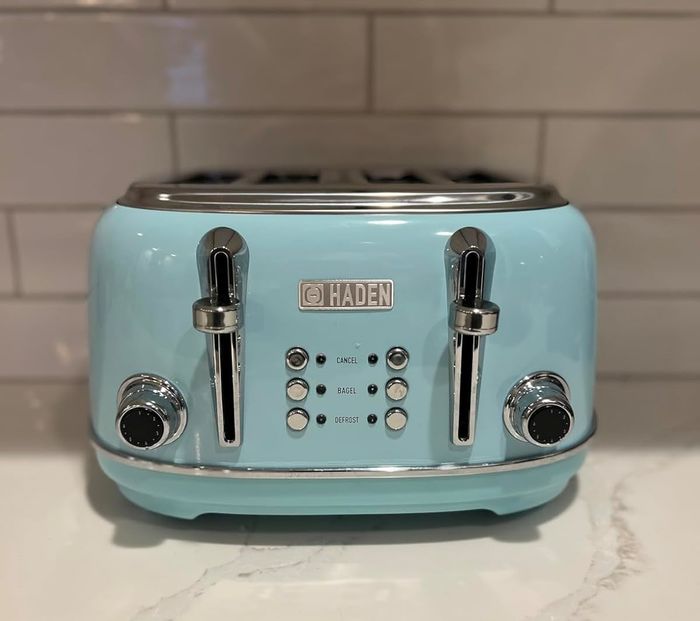 A Haden brand toaster with four slots sits on a kitchen counter, accompanied by a tiled backsplash. The toaster includes settings for cancel, bagel, and defrost to suit your needs