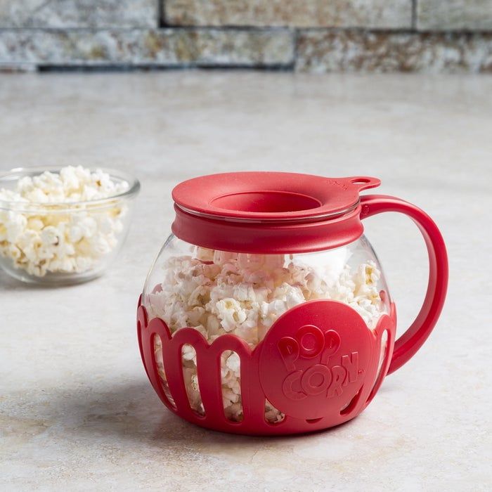 A microwave popcorn maker with a vibrant red silicone lid and handle, overflowing with fresh popcorn, sitting on a kitchen counter.