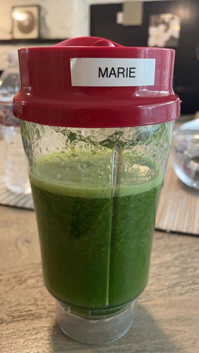 A green smoothie in a blender cup with a red lid labeled.