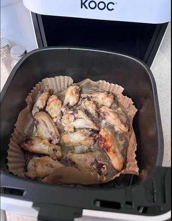 An air fryer with the lid open, showing the cooked food resting inside a liner.