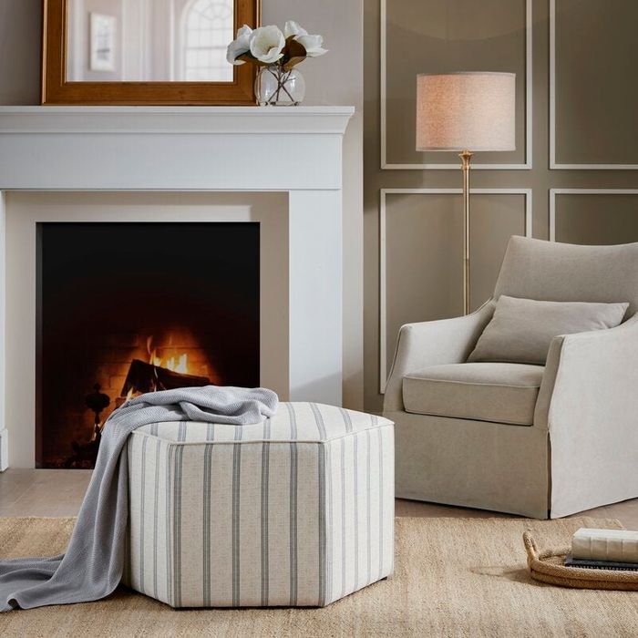A hexagonal ottoman featuring a striking blue and white striped design, positioned elegantly in front of a cozy fireplace.