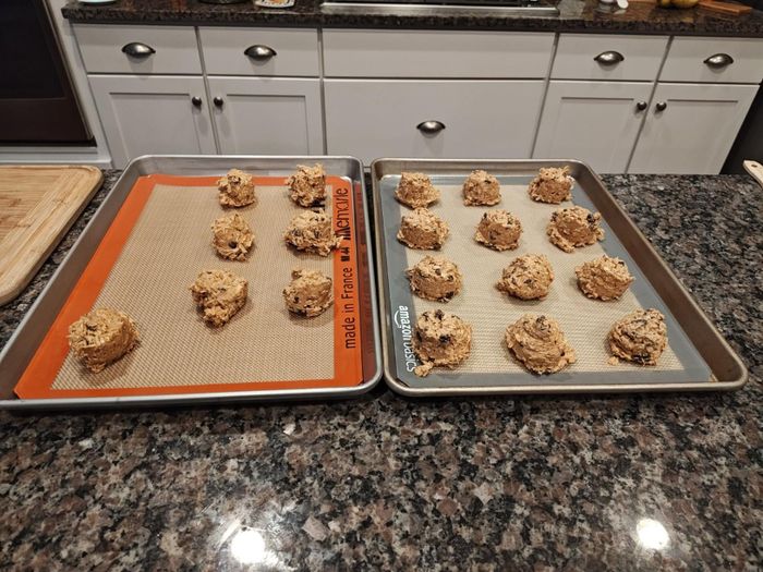 Cookie dough portions neatly arranged on baking trays in a kitchen with granite countertops, ready for the oven.