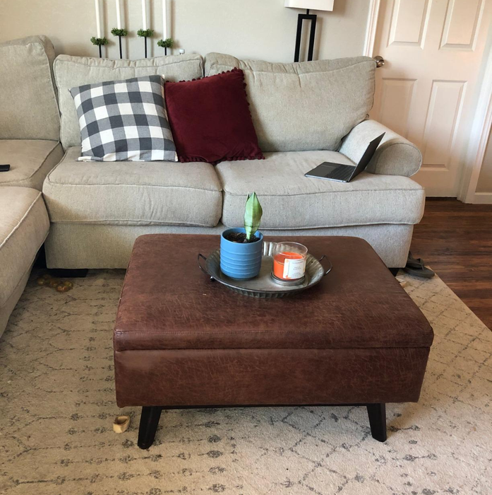 A reviewer's image of a brown faux leather ottoman used as a coffee table