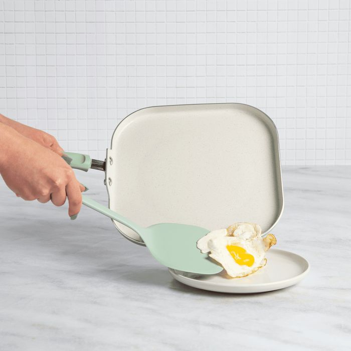 A person slides a perfectly cooked fried egg from the skillet onto a plate using a spatula.